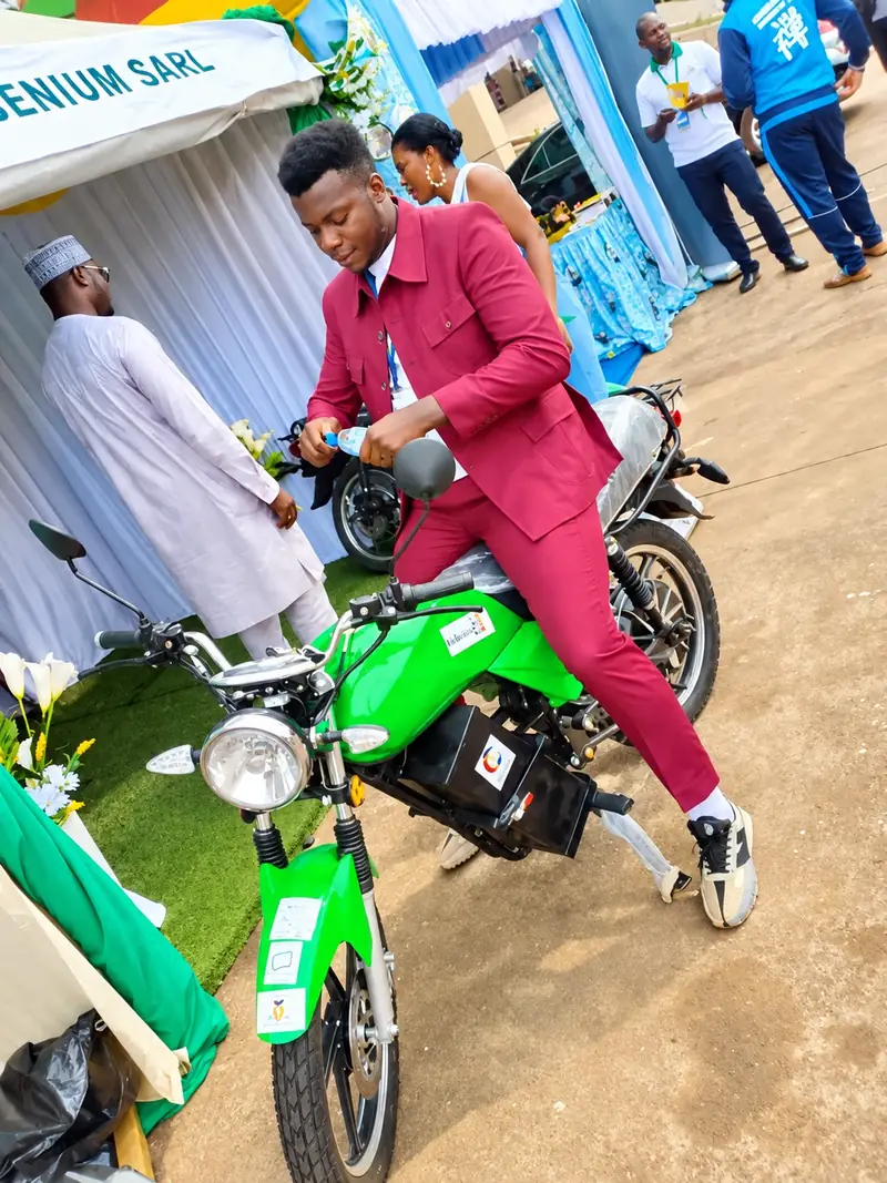 Un membre de l'équipe sur la moto électrique Babana 237 verte, devant le stand Ingenium SARL lors d'un salon