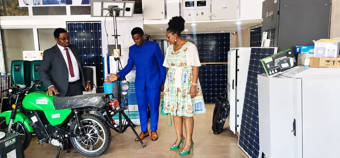 Présentation de la moto Babana 237 à des visiteurs dans le showroom, entre panneaux solaires et équipements